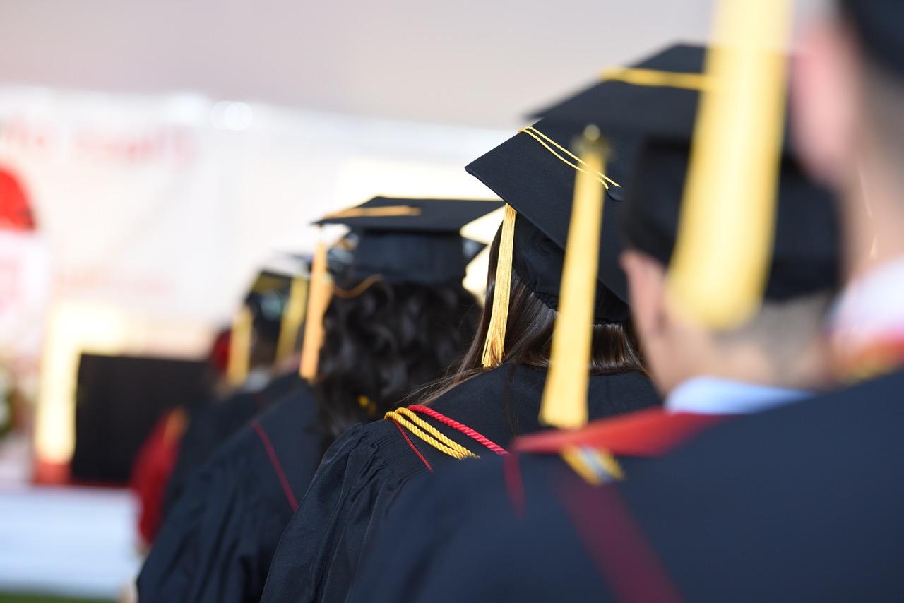 Image is of a line of students sitting at commencement with a view of their graduation caps